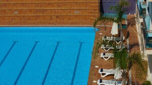 A swimming pool with clear blue water, surrounded by lounge chairs and palm trees.