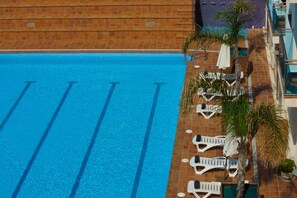 A swimming pool with clear blue water, surrounded by lounge chairs and palm trees.