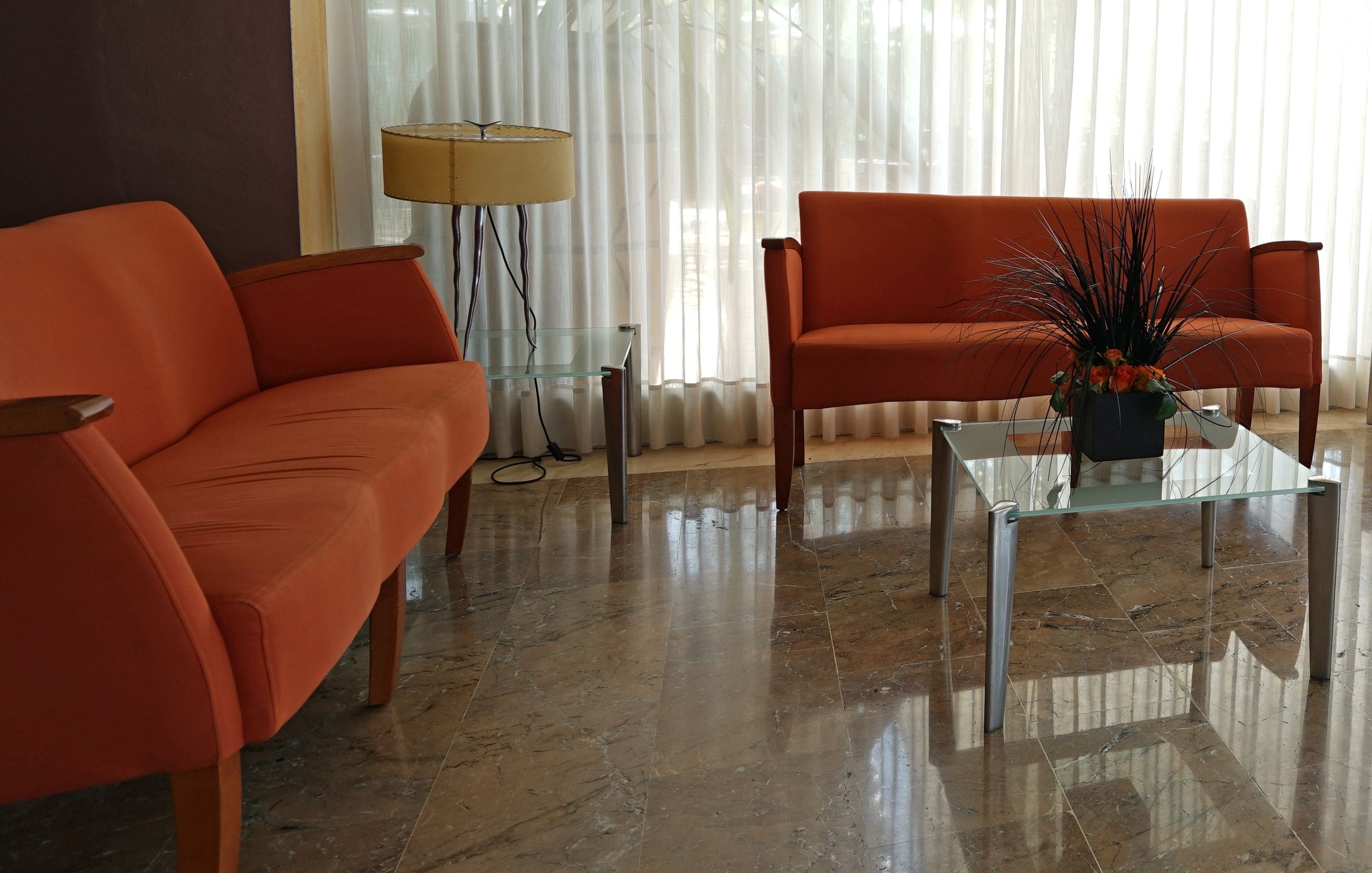 A modern living room with two orange sofas, a glass coffee table, and a floor lamp.