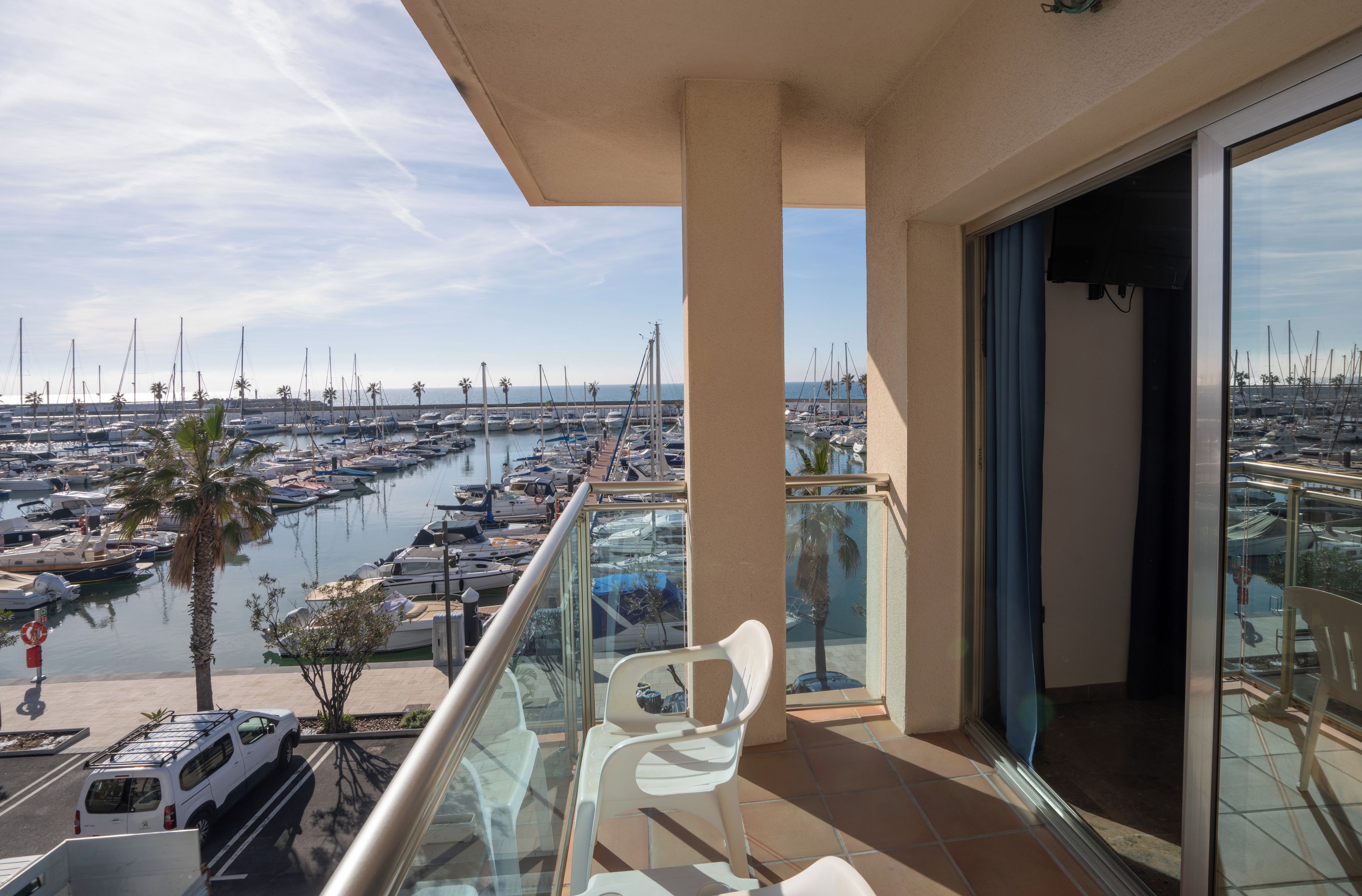 Ein Balkon mit Blick auf eine Marina, Sitzgelegenheiten im Freien und ein geparktes Auto.