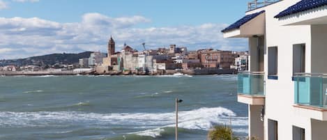 A coastal cityscape with a prominent historical building, a modern building with balconies, and a view of the sea.