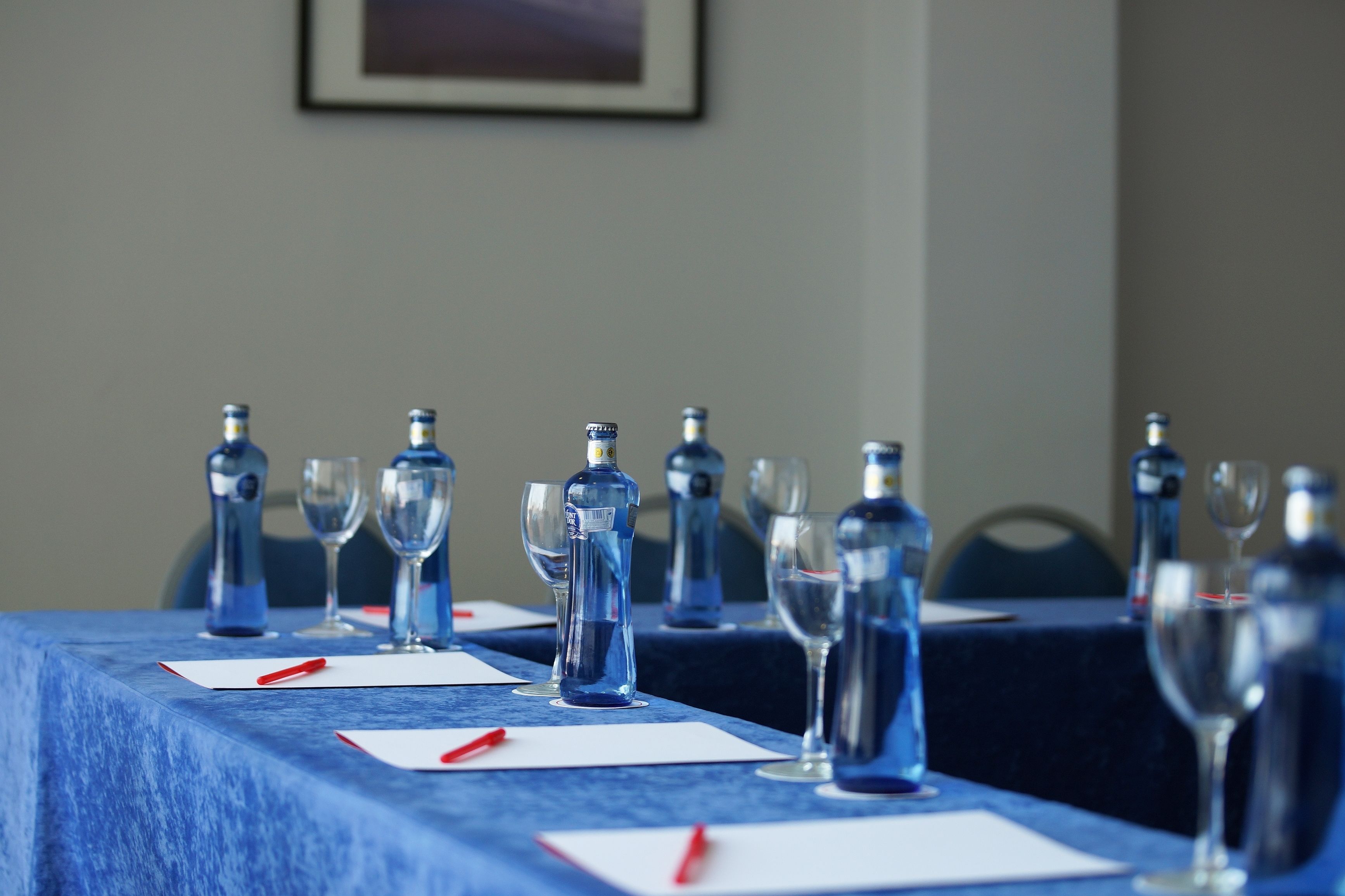 Ein Konferenztisch mit Wasserflaschen und Gläsern, ein gerahmtes Bild an der Wand und einer blauen Tischdecke.
