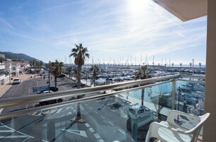 A balcony with a view of a marina, palm trees, and a road with parked cars.