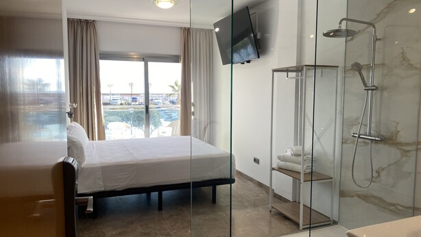 A hotel room with a bed, a shower, and a TV mounted on the wall.