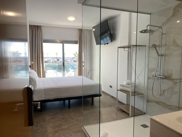 A hotel room with a bed, a shower, and a TV mounted on the wall.
