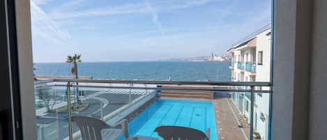 A balcony with a pool, two chairs, and a table.