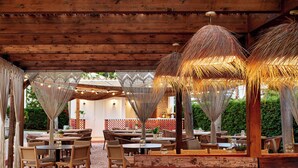Un área de comedor al aire libre con mesas y sillas de madera, rodeada de sombrillas decorativas y luces colgantes.