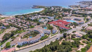 Vista aérea de un pueblo costero con edificios residenciales, un complejo de piscinas y una carretera que lo atraviesa.