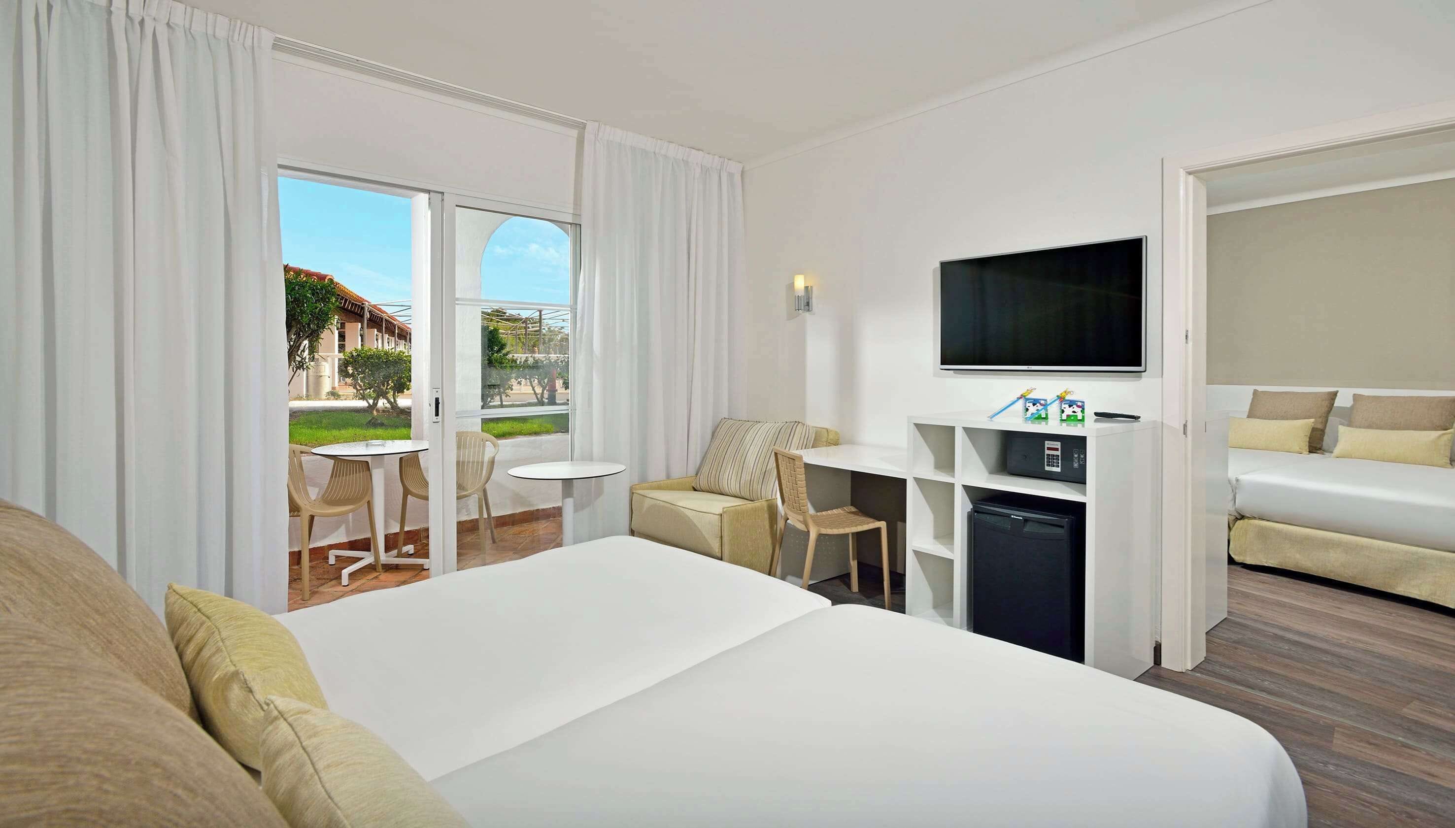 A hotel room with a bed, a desk with a TV, a small fridge, and a seating area with chairs and a table.