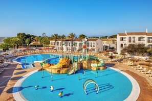 Una gran piscina con toboganes y fuentes, rodeada de sillas de descanso y sombrillas.