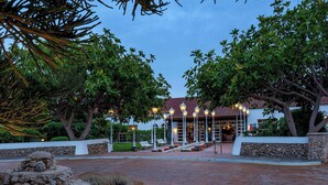Entrada de hotel con un camino de piedra que conduce a un edificio con tejado de baldosas. Hay zonas de estar al aire libre y un jardín bien cuidado.