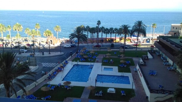 A resort with a swimming pool, lounge chairs, palm trees, and a view of the sea. - Aloha Playa (BENALMADENA)