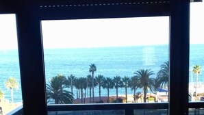 A balcony with a table and chairs, overlooking a beach with palm trees and the sea. - Aloha Playa (BENALMADENA)