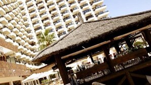 A high-rise hotel with multiple balconies, a thatched-roof structure, and a pool area. - Aloha Playa (BENALMADENA)