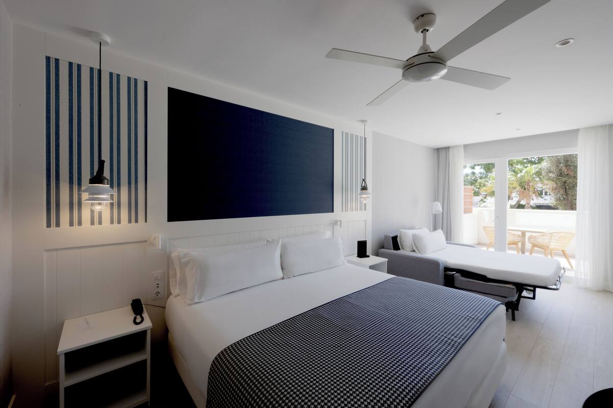 A modern hotel room with a large bed, a ceiling fan, a small desk, and a balcony with a view.