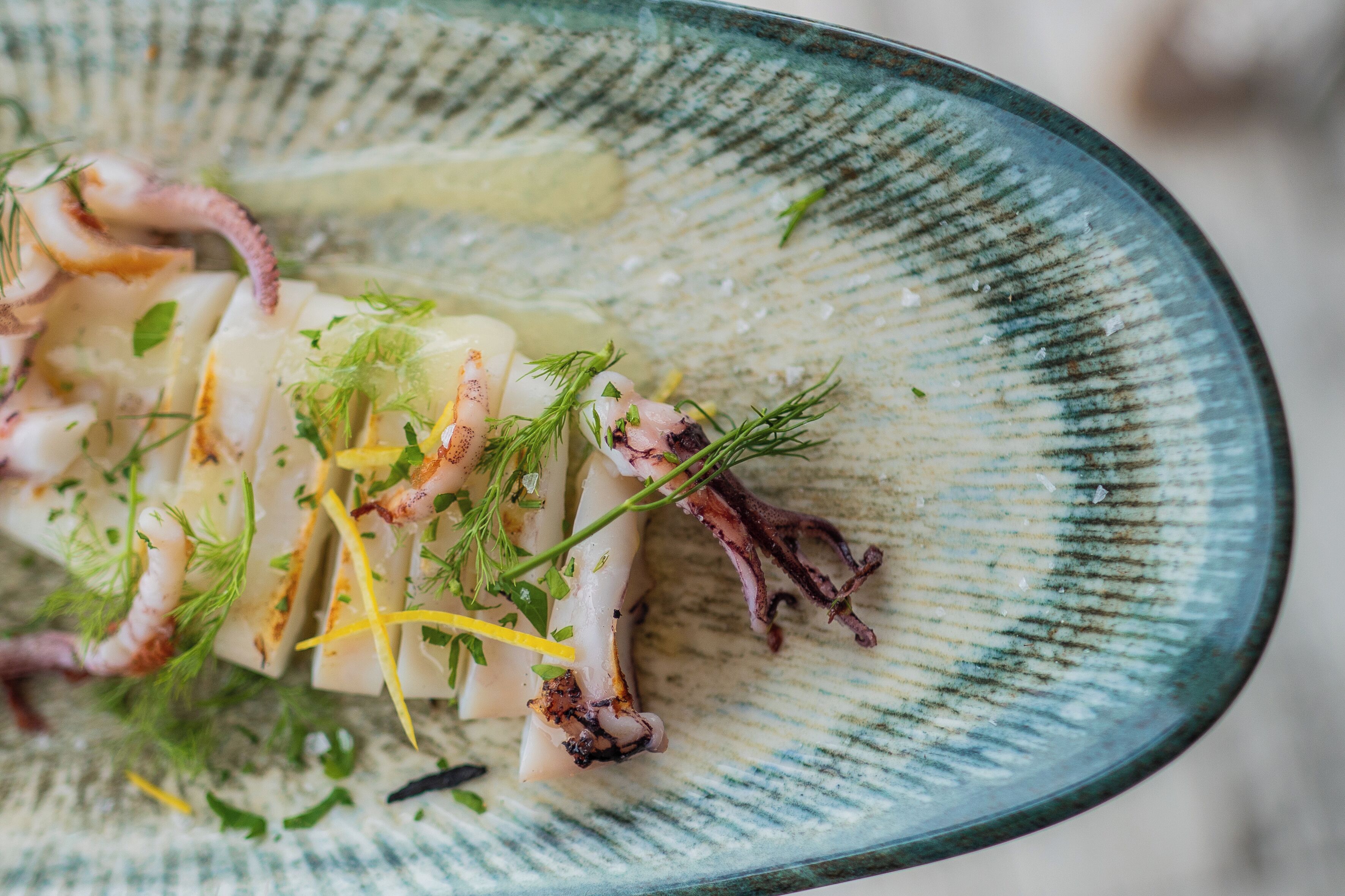 A plate of food with octopus, lemon, and herbs.
