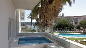 A modern outdoor swimming pool with a glass balustrade, a palm tree, and a view of a historic building in the background. - Catalonia Mirador des Port (Mahón)