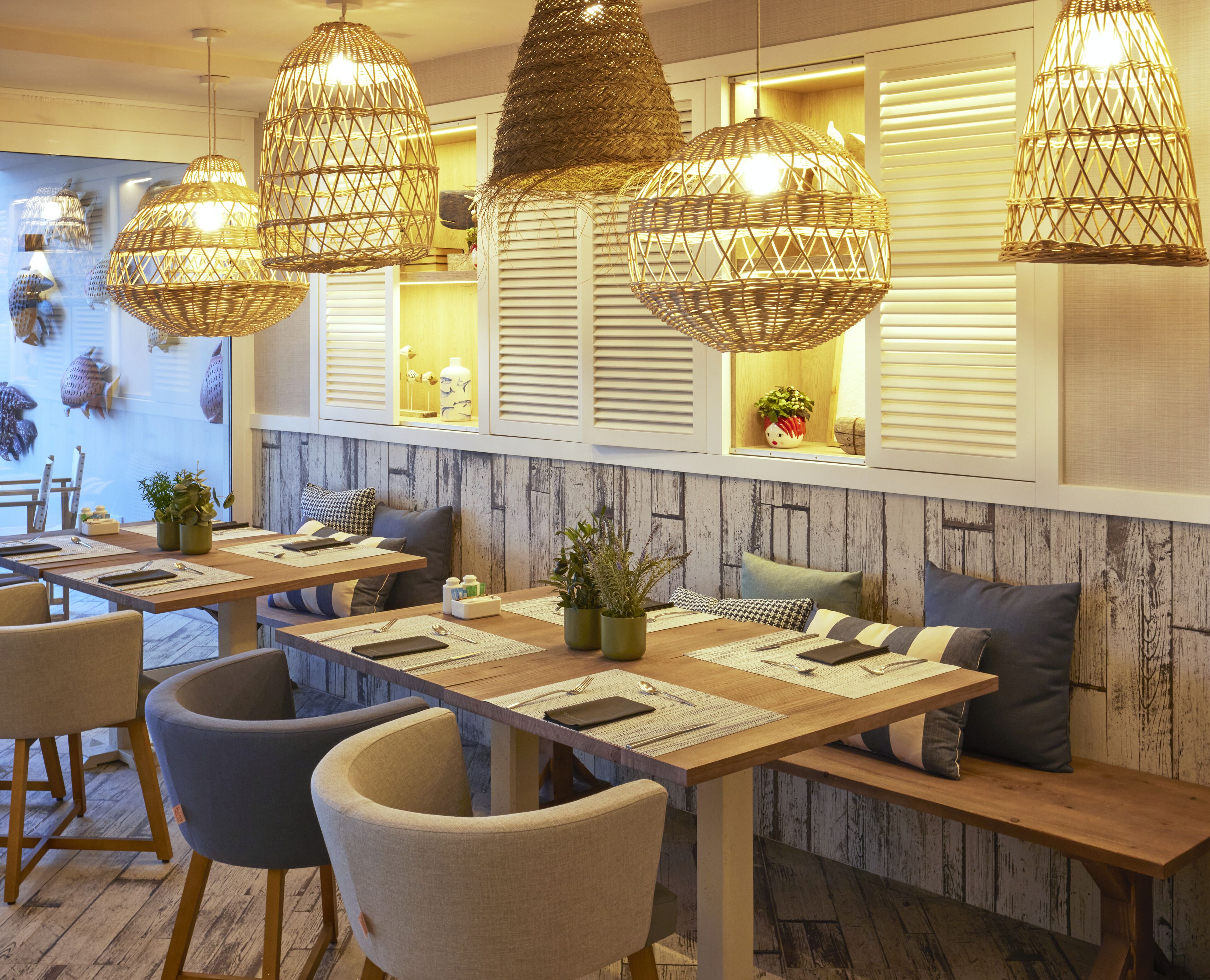 A restaurant interior with wooden tables, cushioned chairs, and woven pendant lights.