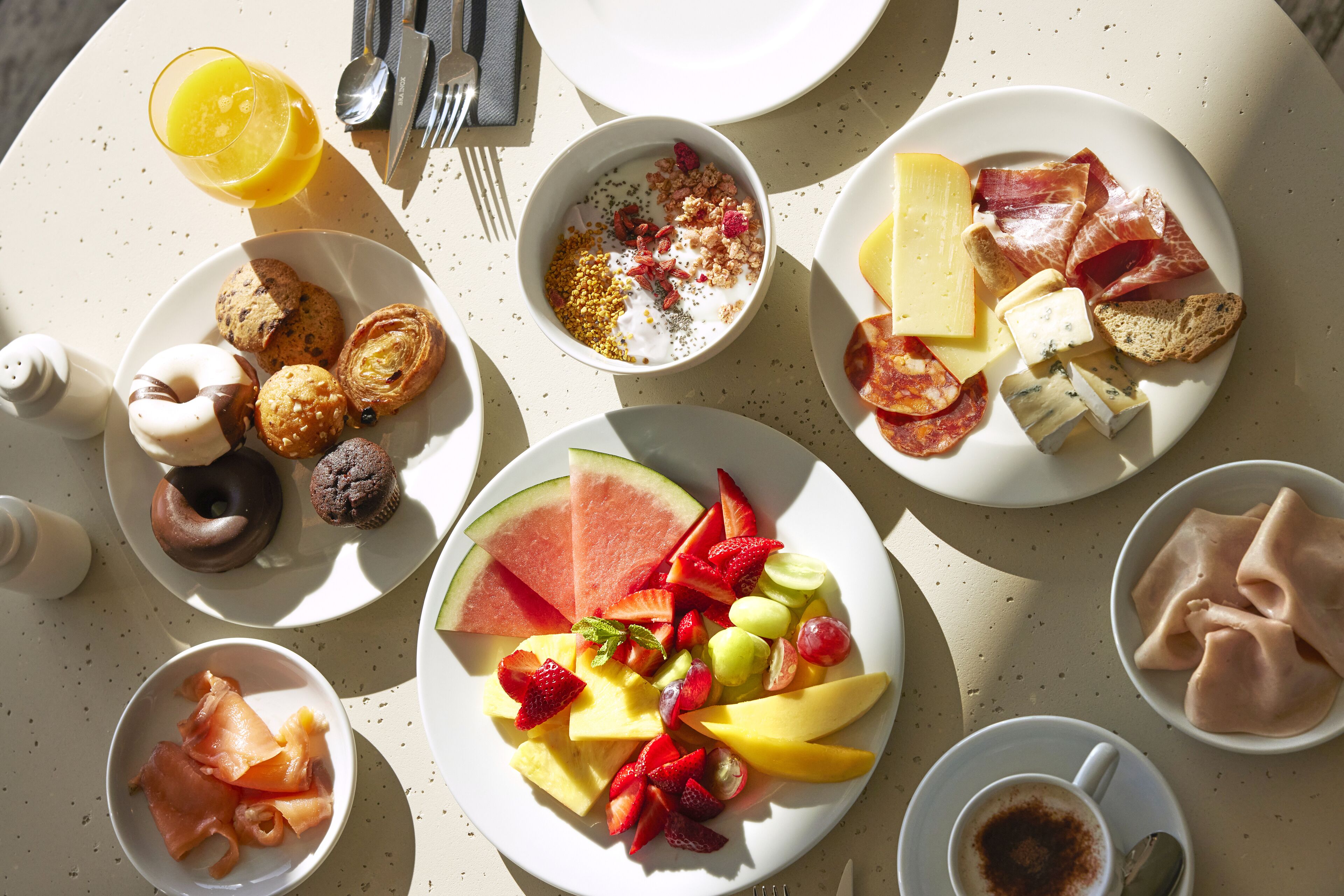 Una mesa de desayuno con diversos alimentos, incluyendo pasteles, frutas, queso y embutidos.