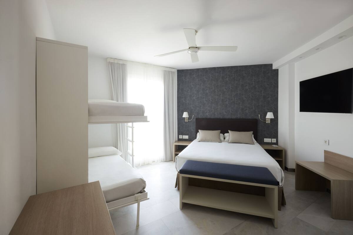 A modern hotel room with a large bed, a desk, a ceiling fan, and a TV mounted on the wall.