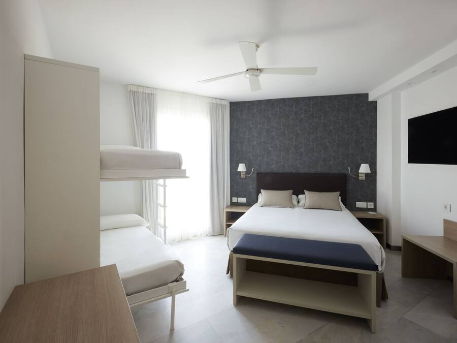 Une chambre d’hôtel moderne, dotée d’un grand lit, d’un bureau, d’un ventilateur de plafond et d’un téléviseur fixé au mur.