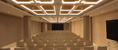 A conference room with rows of chairs, a large screen, and a ceiling with geometric lighting.