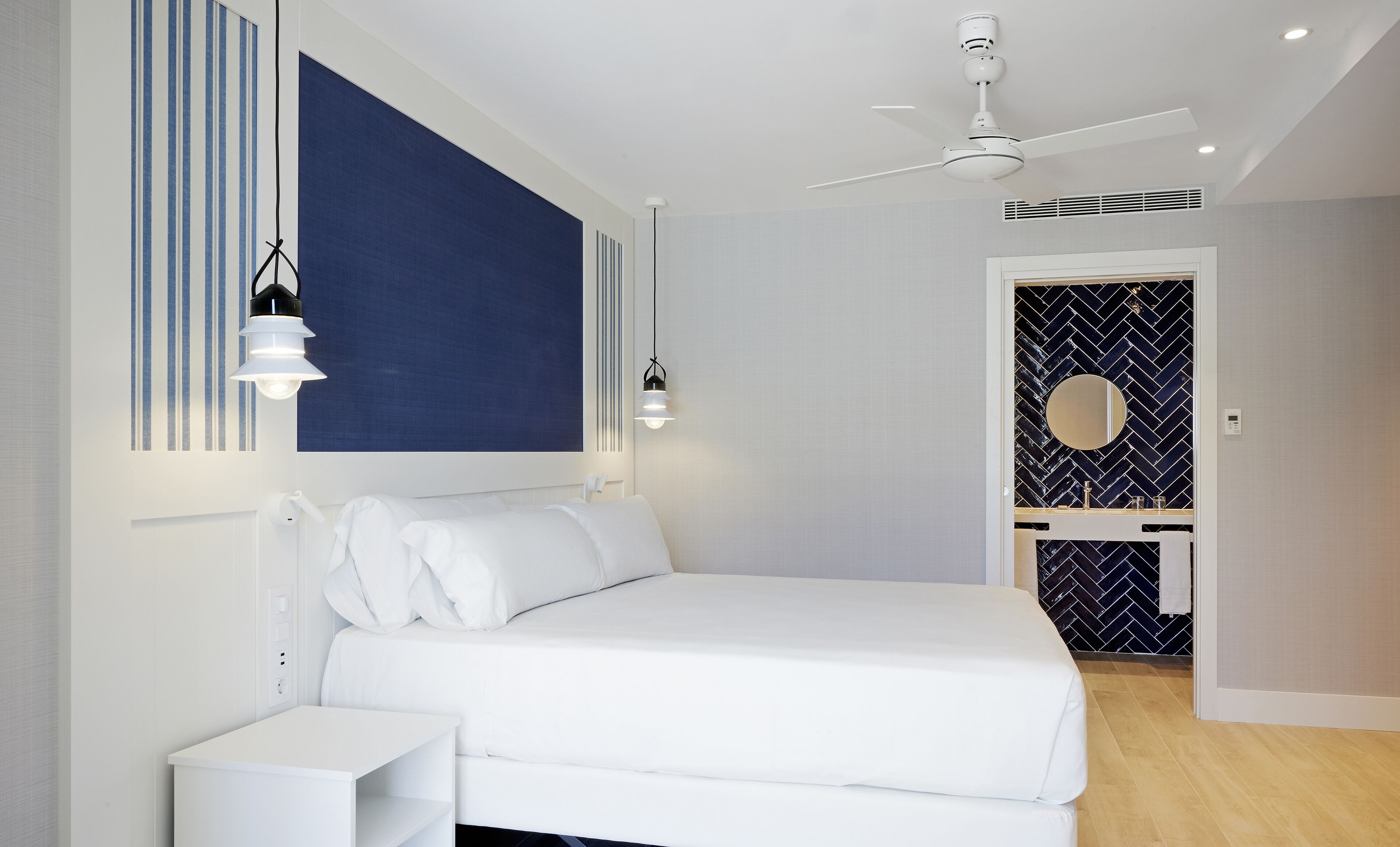 Ein modernes Schlafzimmer mit Bett, Nachttischen, Deckenventilator und einem Badezimmer mit Spiegel und Waschbecken.