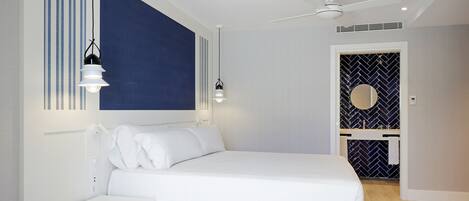 Ein modernes Schlafzimmer mit Bett, Nachttischen, Deckenventilator und einem Badezimmer mit Spiegel und Waschbecken.