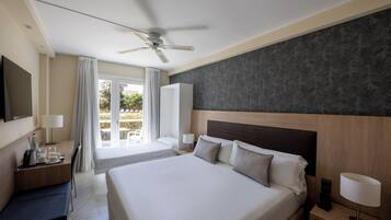 Une chambre d’hôtel avec un grand lit, un bureau avec une chaise, une télévision, un ventilateur de plafond et une fenêtre avec des rideaux.