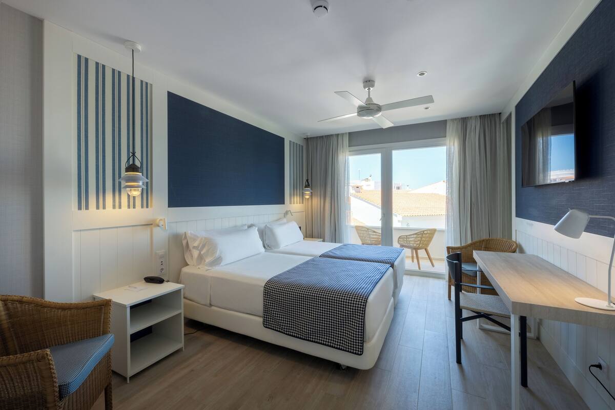 A modern hotel room with a large bed, a desk, a chair, and a balcony with a view.