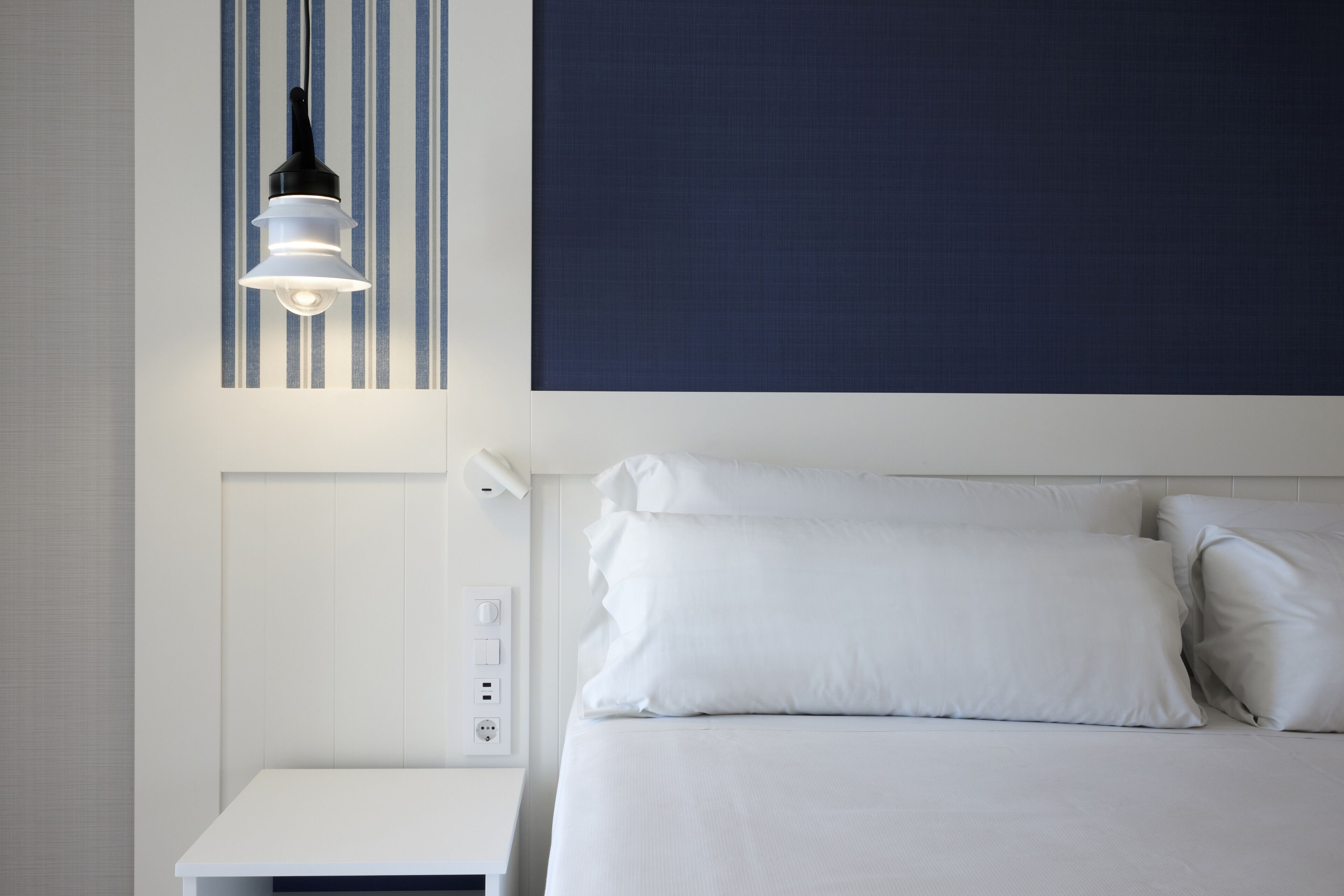 A neatly arranged hotel room with a bed, a bedside table, and a wall-mounted light fixture.