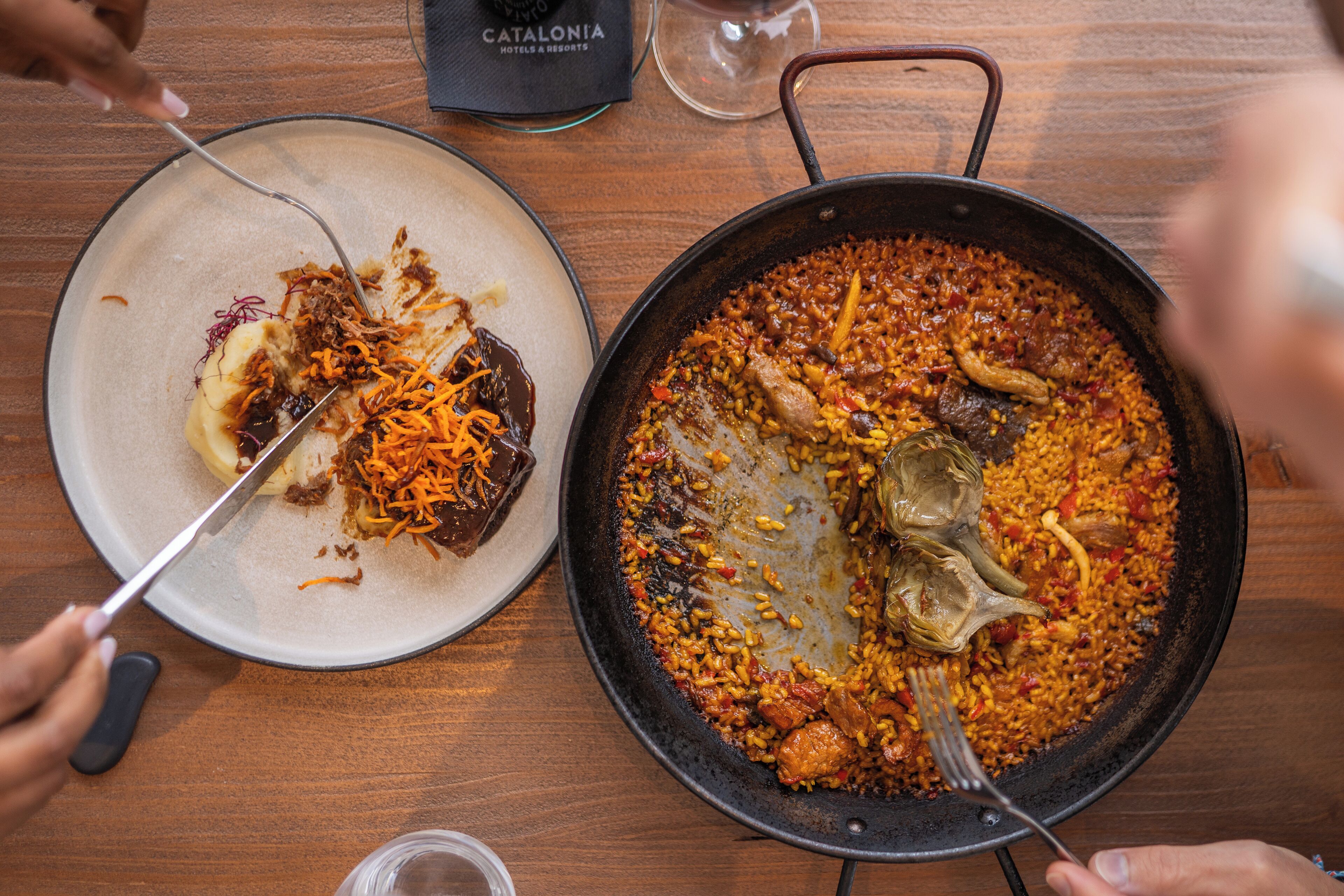 A dining table with a pan of paella and a plate with food remnants.