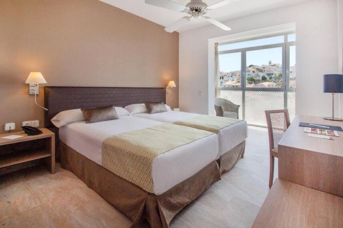 A hotel room with a bed, bedside tables, a desk, and a chair.
