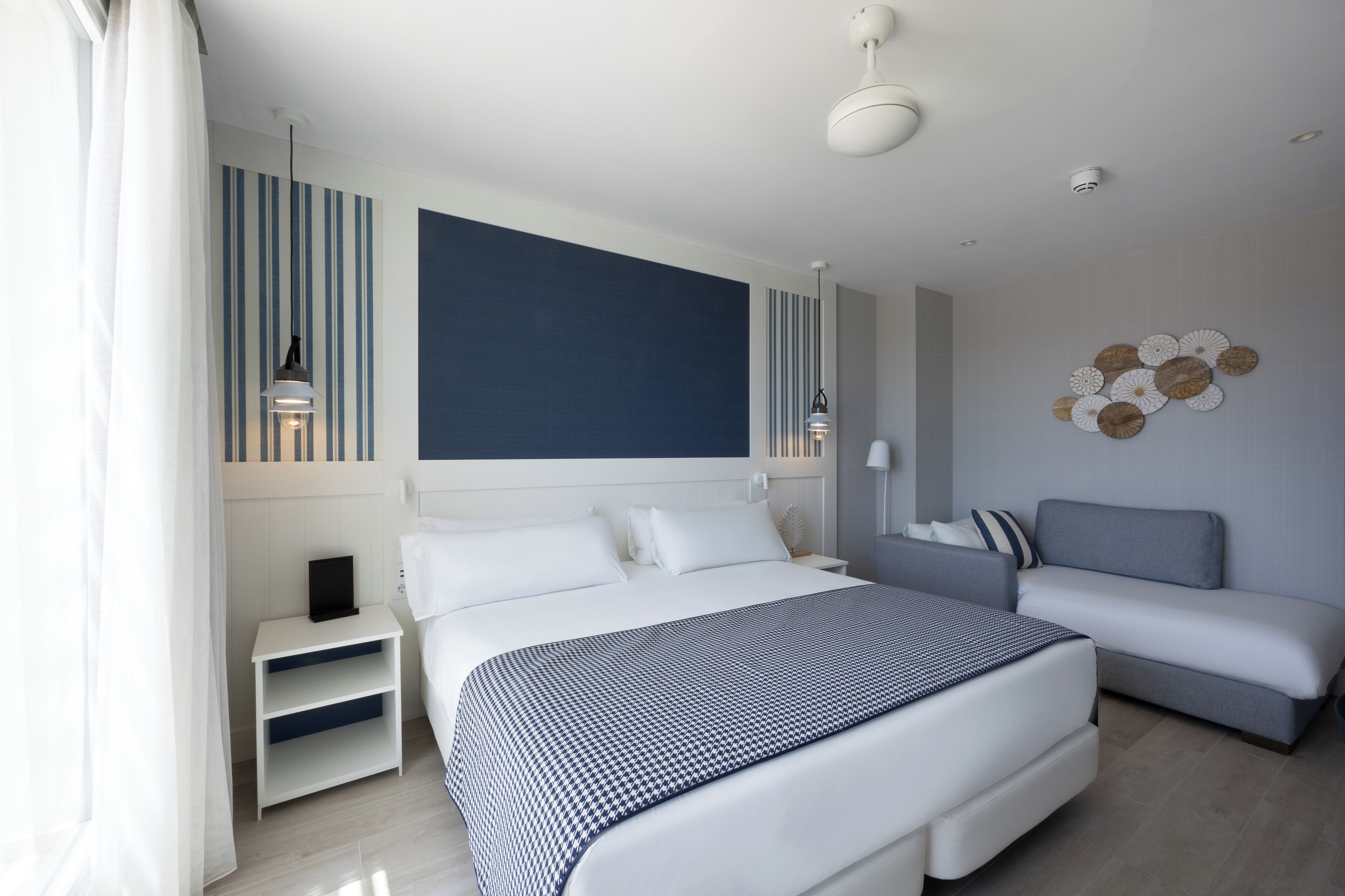 A modern hotel room with a large bed, a sofa, a nightstand, and a decorative wall piece.