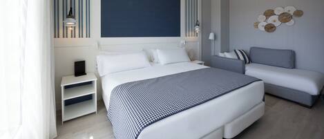 A modern hotel room with a large bed, a sofa, a nightstand, and a decorative wall piece.
