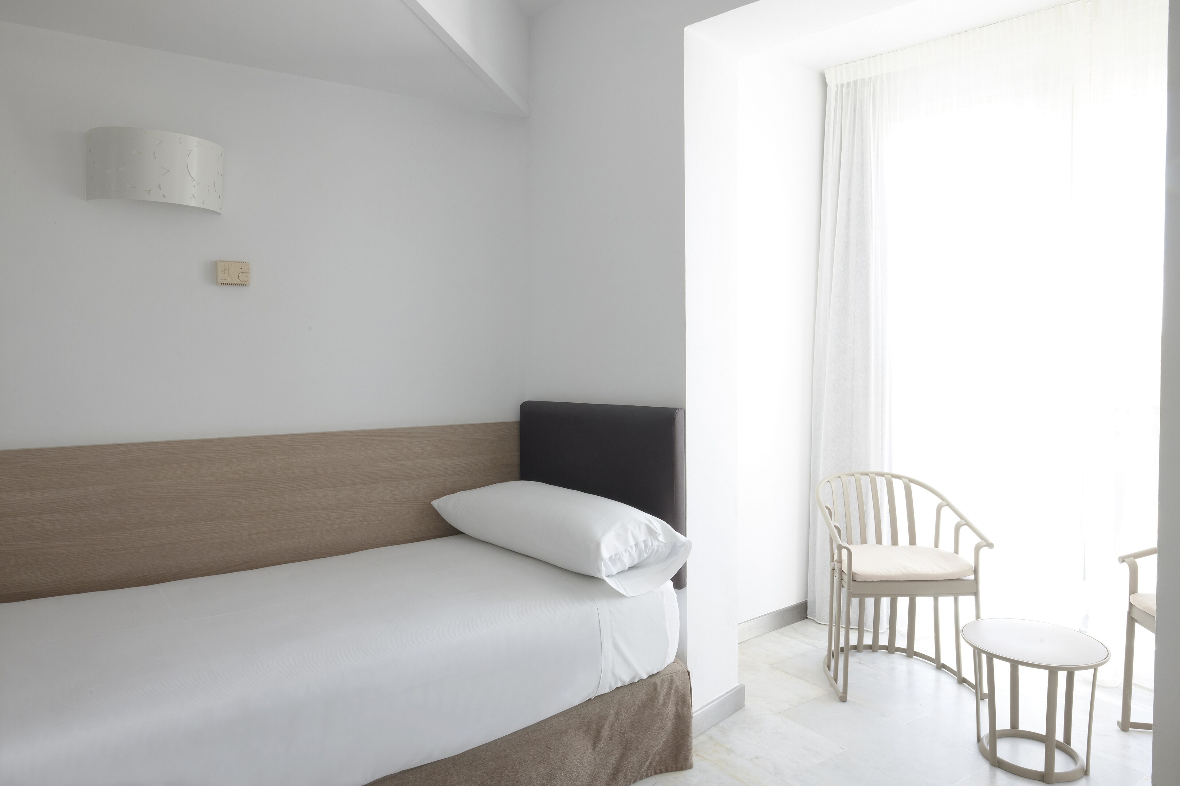 Une chambre d’hôtel minimaliste, avec un lit simple, une petite table et une chaise.