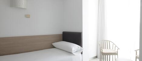 Une chambre d’hôtel minimaliste, avec un lit simple, une petite table et une chaise.