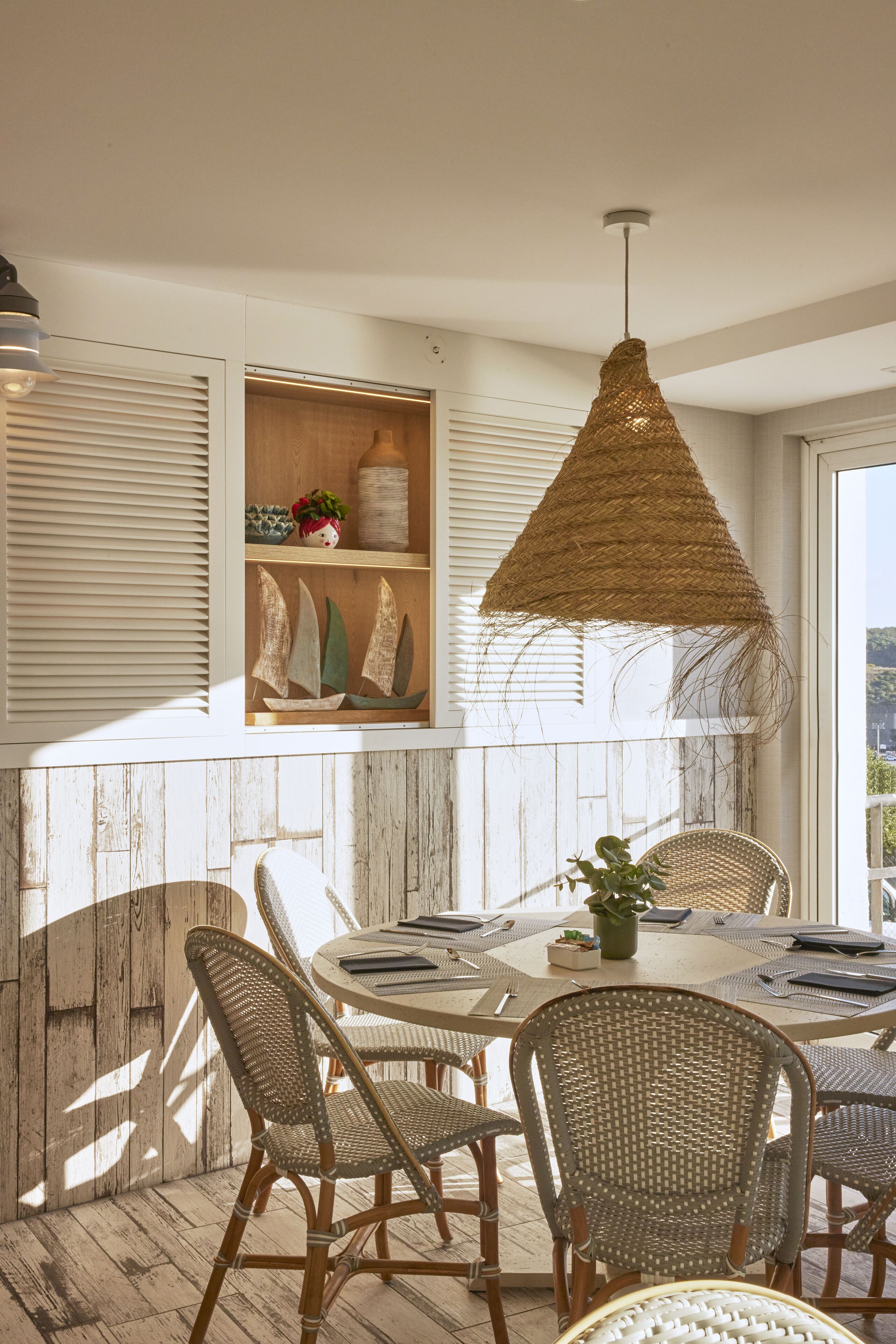 Un coin repas avec des chaises en osier, une table ronde et un luminaire suspendu.