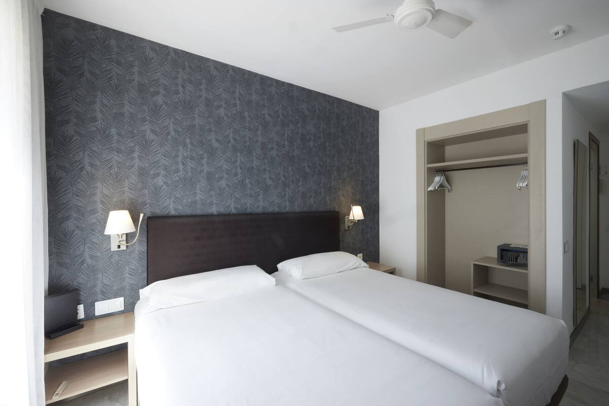 A hotel room with a large bed, two bedside tables, a wardrobe, and a ceiling fan.