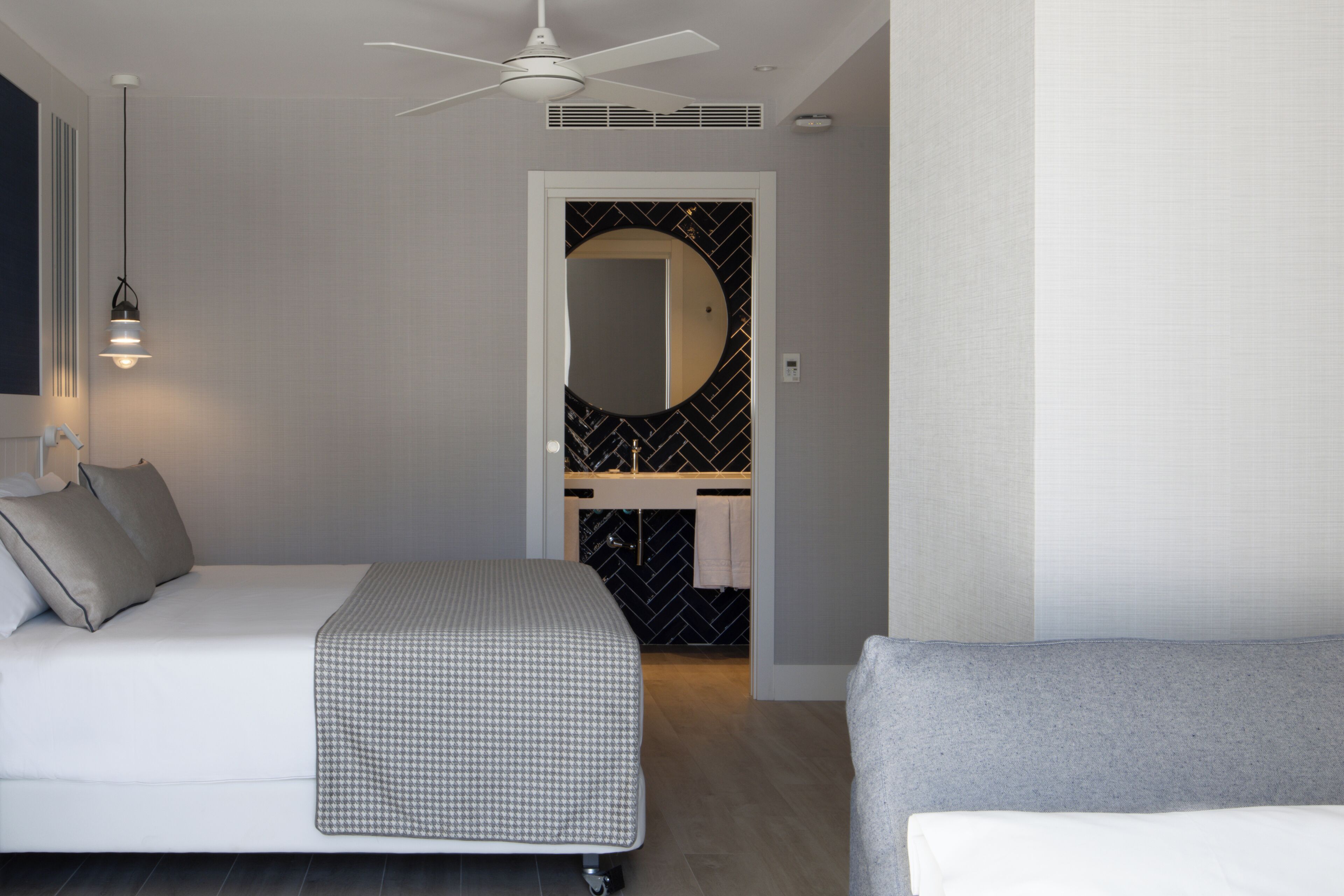 Ein modernes Schlafzimmer mit Bett, Deckenventilator, Nachttischlampe und einem Badezimmer mit Spiegel und Waschbecken.