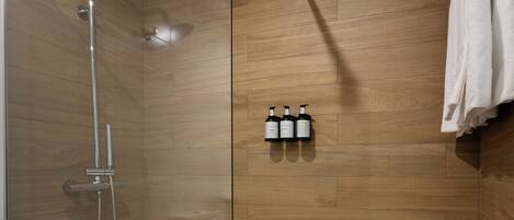 A glass-enclosed shower with a wooden floor, a towel hanging on the wall, and three bottles of shampoo.