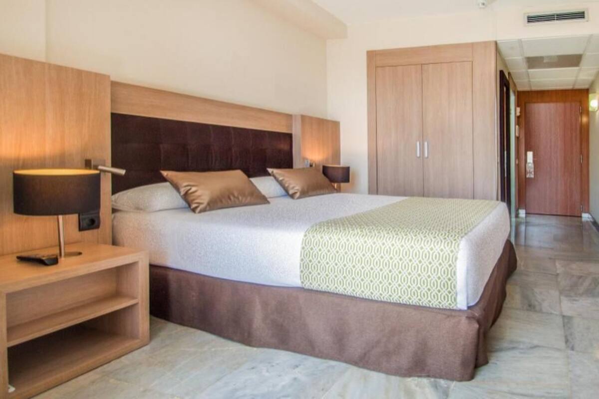 A hotel room with a bed, bedside tables, a wardrobe, and a television.