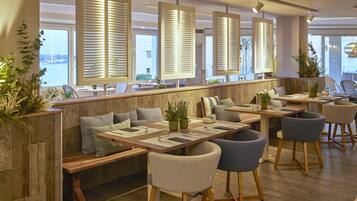 Un restaurante moderno con mesas de madera, asientos acolchados y grandes ventanales con persianas.