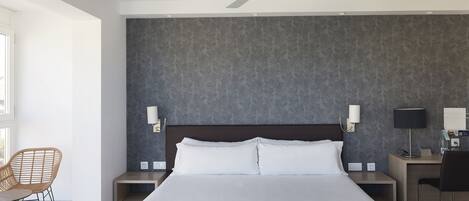 Habitación de hotel con una cama grande, ventilador de techo, escritorio con silla y lámpara de pared.