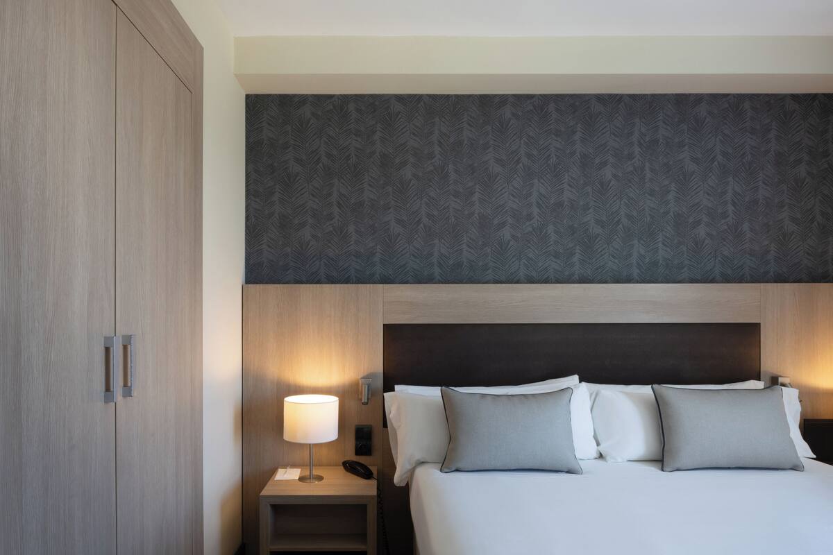 A hotel room with a large bed, a nightstand with a lamp, and a wardrobe.