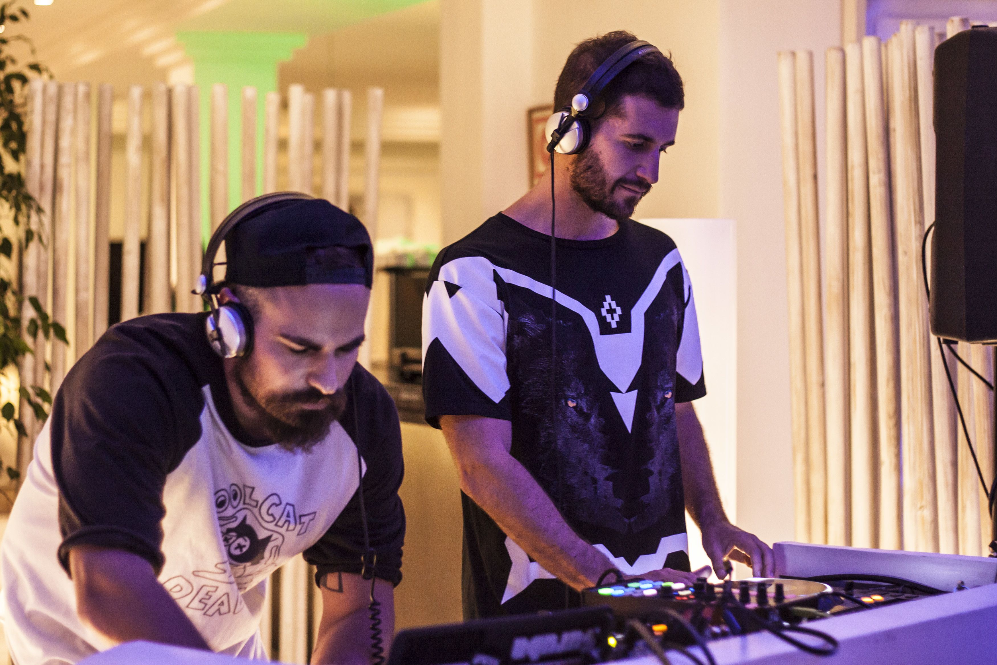 Deux personnes manipulent du matériel de DJ dans une pièce aux murs recouverts de lambris en bois verticaux et au design moderne.