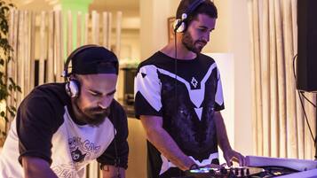 Two individuals operating DJ equipment in a room with vertical wooden slats and a modern design.