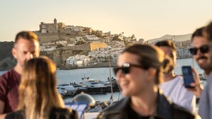 A coastal town with a historic castle on a hill, boats docked at a marina, and people in the foreground. - Ocean Drive Ibiza (Ibiza Town)