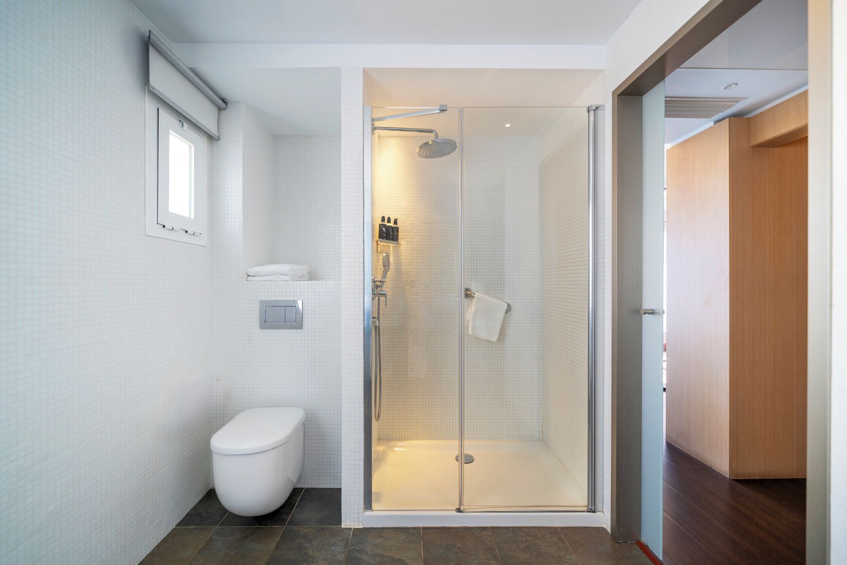 Un baño moderno con cabina de ducha de vidrio, un inodoro y un pequeño estante con artículos de aseo.