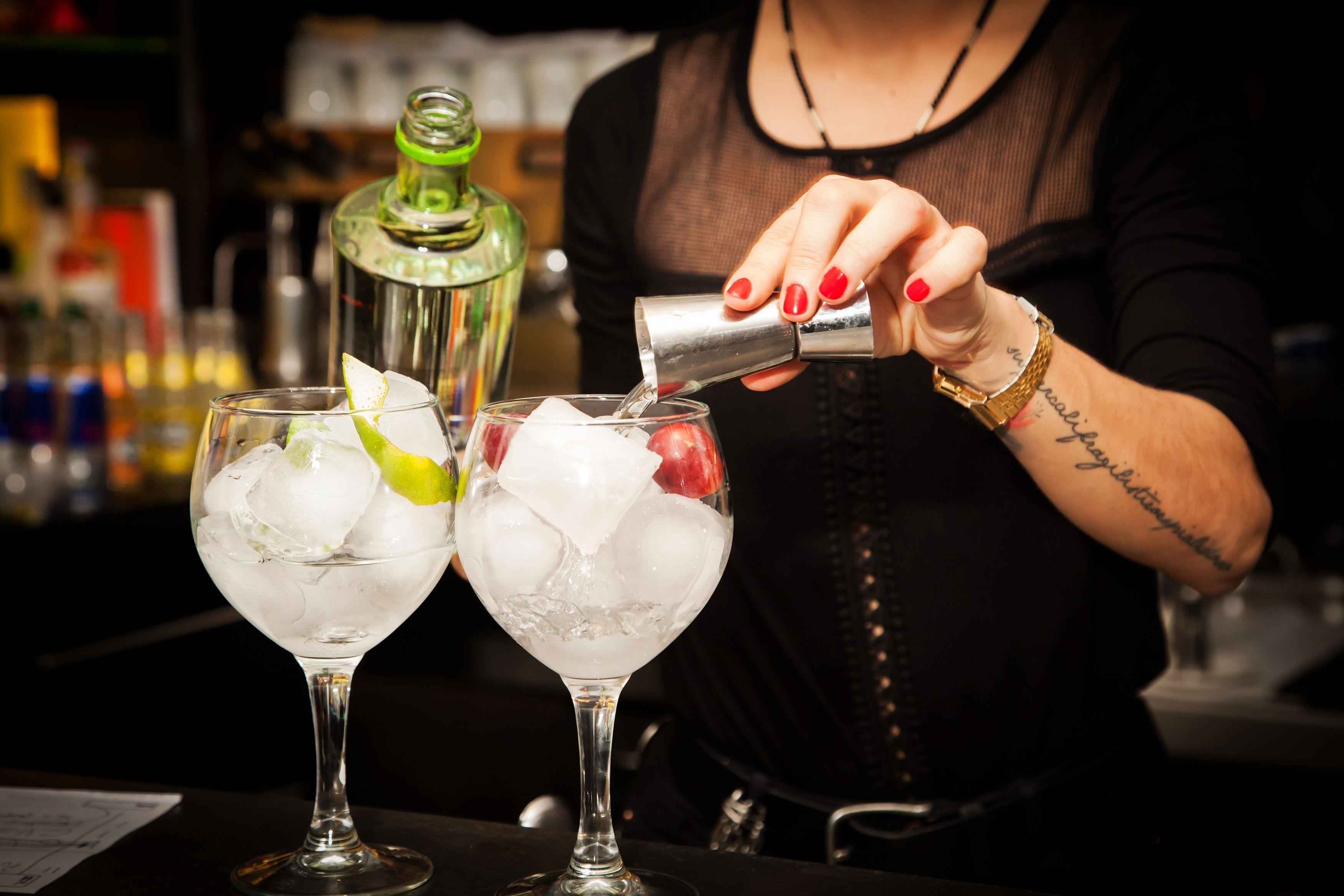 Ein Barkeeper gießt ein Getränk in ein Glas mit Eiswürfeln und einem Limettenschnitz.